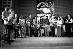 Black-and-white image of adults standing with their children at the front of the Great Hall, Rogue Valley Unitarian Universalist Fellowship
