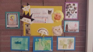 Grouping of student artwork, including collage, watercolor, pencil coloring and animal masks cut out of paper plates around a sign that reads, 'Save the Endangered Animals!'