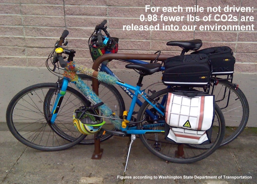 Two bicycles locked to bicycle rack. Text in upper-right corner of image reads, ''For each mile not driven: 0.98 fewer lbs of CO2s are released into our environment.' Text in lower-right corner of graphic reads: 'Figures according to Washington State Department of Transportation'